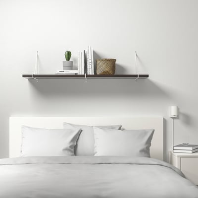 Minimalistisches weißes Schlafzimmer mit BERGSHULT-Wandregal mit Büchern, Pflanzen und Korb über einem ordentlich gemachten Bett mit weißer Bettwäsche.