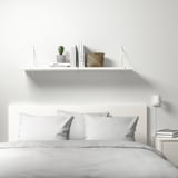 Minimalistisches Schlafzimmer mit BERGSHULT Wandregal für Bücher, Pflanzen und Korb. Saubere weiße Linien.