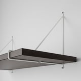 Schwarzes rechteckiges Wandregal mit weißen Metallhalterungen, die an einer weißen Wand befestigt sind. Die Befestigung des Regals erfolgt mit sichtbaren Schrauben.