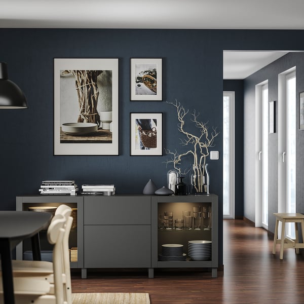 Modernes Esszimmer mit dunkelgrauem BESTÅ-Stauraum, weiß gerahmter Kunst und Holztisch.