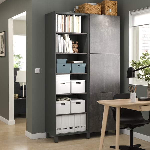Modernes Home Office mit schwarzem BESTÅ-Bücherregal mit Aufbewahrungsboxen und Büchern, neben einem Holzschreibtisch mit Stuhl.