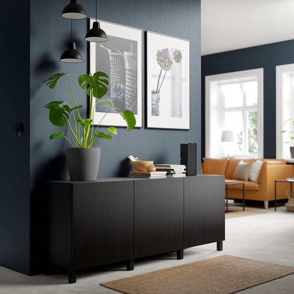 Modernes Wohnzimmer mit schwarzem BESTÅ Sideboard, Pflanze, orangefarbenem Sofa und minimalistischem Dekor.