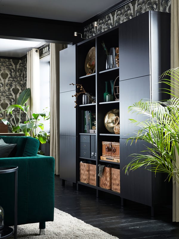 Modernes Wohnzimmer mit schwarzen create & BESTÅ Aufbewahrungseinheiten, grünem Sofa, dekorativen Vasen und Wandpflanzen.