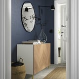 Kleiner Eingangsbereich mit blauer Wand, hellem Holzschrank, schwarzem Spiegel, Hängelampe, geflochtenem Korb und Türansicht.