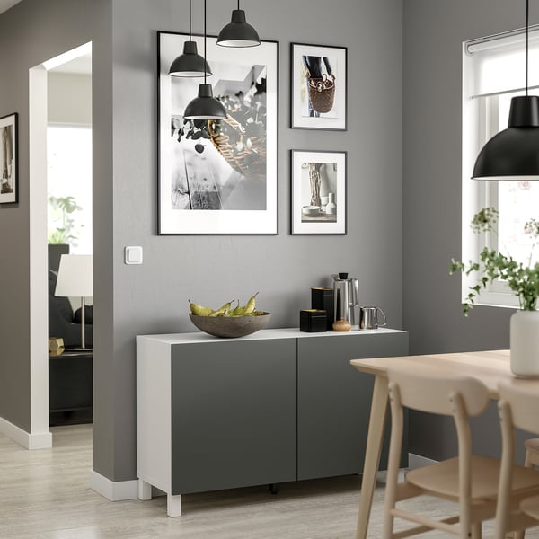 Modernes Wohnzimmer mit grauem BESTÅ-Stauraum, weißer Platte, schwarzen Pendelleuchten, gerahmten Fotos und Holzstühlen.