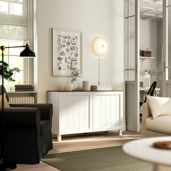 BESTÅ weißes Sideboard mit Türen und Regalen an der Wand, Kunst, Licht, Stuhl, Pflanze, Teppich, Dekoration, Vase, Bücher.