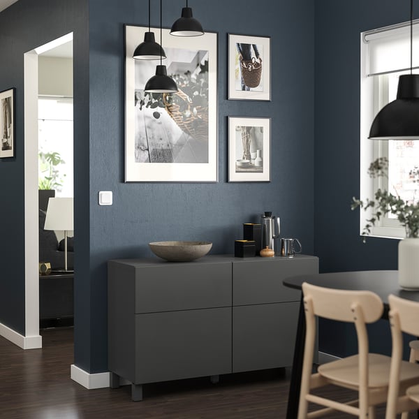 Dunkelgrauer BESTÅ-Schrank, weißes Dekor, Kunstwerk, Holzstühle, schwarze Lichter, marineblaue Wände.