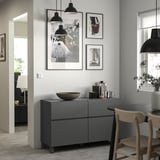 Moderner Wohnraum mit grauem BESTÅ-Stauraum mit Pendelleuchten, gerahmter Kunst und Holzstühlen.