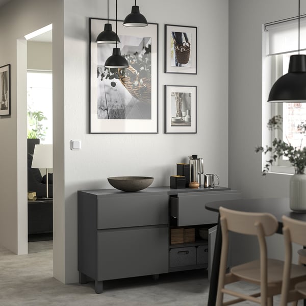 Modernes Wohnzimmer mit grauem BESTÅ-Stauraum, schwarzen Pendelleuchten, Holzstühlen und gerahmter Wandkunst.