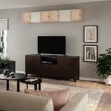 Modernes Wohnzimmer mit BESTÅ TV-Möbel und Korbtüren, dunkelbraun, vor grauer Wand, Kunst, Pflanze, schwarzem Couchtisch, beigem Sofa.