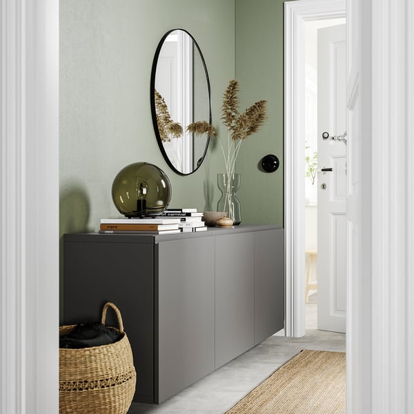Moderner Eingangsbereich mit grünen Wänden, grauem BESTÅ-Schrank, ovalem Spiegel, getrockneten Pflanzen, Lampe und Korb.