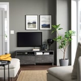 Modernes Wohnzimmer mit einem BESTÅ-TV-Ständer in Grau mit einem Flachbildfernseher, der mit Büchern, Pflanzen und gerahmten Bergfotos gestaltet ist.