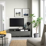 Modernes Wohnzimmer mit BESTÅ-TV-Bank, Flachbildfernseher, weißem Sofa, gelber Decke, grüner Pflanze, Bergfotos, grauem Teppich, schwarzer Lampe, Büchern.