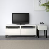 Weiße BESTÅ TV-Bank mit Flachbildschirm, 2 Schubladen, DVD-Player, Kopfhörer, Buch auf kleinem Tisch, minimalistisches Zimmer.