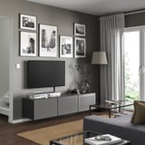 Modernes Wohnzimmer mit grauer BESTÅ-TV-Bank, Flachbildfernseher, Schwarz-Weiß-Fotos, grauen Vorhängen, Holzboden und Couchtisch aus Glas.
