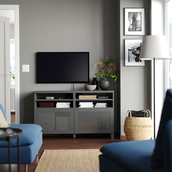 Modernes Wohnzimmer mit grauer BESTÅ-TV-Konsole, blauer Couch, Flachbildfernseher, geflochtenem Korb und zwei gerahmten Fotos an einer grauen Wand.