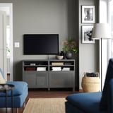 Modernes Wohnzimmer mit grauer BESTÅ-TV-Konsole, blauer Couch, Flachbildfernseher, geflochtenem Korb und zwei gerahmten Fotos an einer grauen Wand.