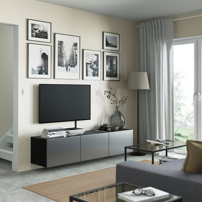 Modernes Wohnzimmer mit BESTÅ-TV-Bank, Flachbildfernseher, Büchern, Vase und grauen Vorhängen.