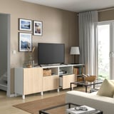 Modernes Wohnzimmer mit hellem Holz-TV-Ständer, Flachbildfernseher, Lampe in der Nähe und gerahmten Bildern an der Wand.