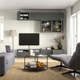 Dunkelgraue BESTÅ TV-Bank mit Sofa, Couchtisch, Schränken, Kissen, Büchern und Vase.