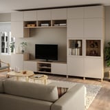 Modernes Wohnzimmer mit BESTÅ-Stauraum und TV. Neutrale Töne, graues Sofa, Holzmöbel, großer Fernseher, natürliches Licht durch Jalousien.