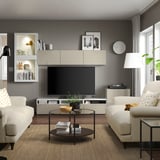 Modernes Wohnzimmer mit hellen Möbeln, großem Fernseher, Sofas, Couchtisch und Pflanzen.