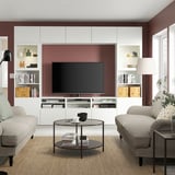 Modernes Wohnzimmer mit BESTÅ-TV, burgunderroten Wänden, beigen Sofas und gemütlicher Beleuchtung.