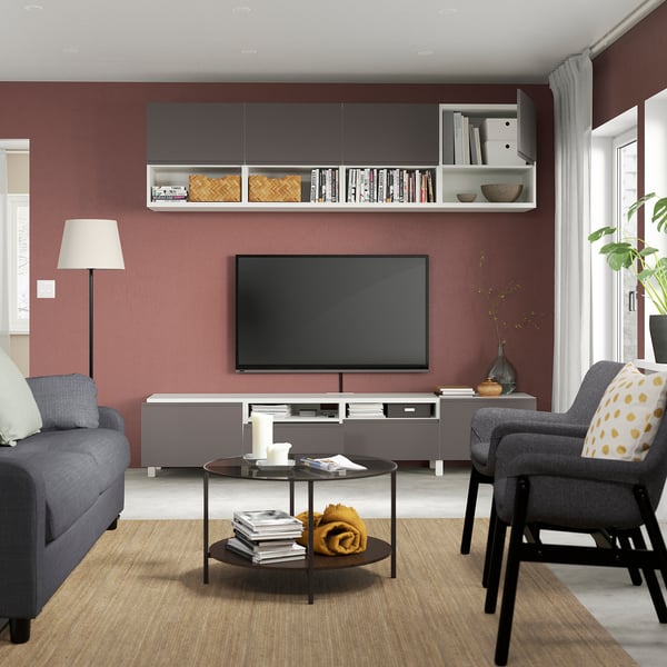 Modernes Wohnzimmer: rote Wand, graues Sofa, Fernseher, Couchtisch mit Dekor, Sessel, Fenster, Lampe, Regale.