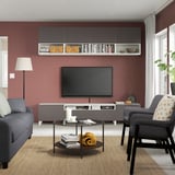 Modernes Wohnzimmer mit kastanienbrauner Akzentwand, TV auf der BESTÅ-Einheit, Sofas, Couchtisch und Pflanze.