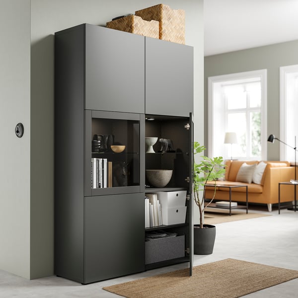 Modernes Wohnzimmer mit schwarzem BESTÅ-Aufbewahrungsschrank, dekorativen Schalen, Büchern und einem geflochtenen Korb. Orangefarbenes Sofa und Pflanze.