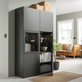 Modernes Wohnzimmer mit schwarzem BESTÅ-Aufbewahrungsschrank, dekorativen Schalen, Büchern und einem geflochtenen Korb. Orangefarbenes Sofa und Pflanze.