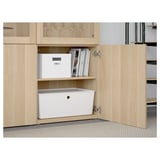 Offener Holzschrank mit organisierter Aufbewahrung. Das untere Regal hat einen großen weißen Mülleimer; Das obere Regal bietet Platz für weiße Box und Zeitschriften. Glastüren oben.