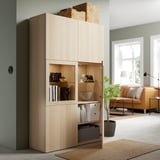 Holzschrank mit Glastüren, in dem Dekorationsgegenstände und Bücher ausgestellt sind. Eine geöffnete Tür zeigt verstellbare Regale und Aufbewahrungsboxen.