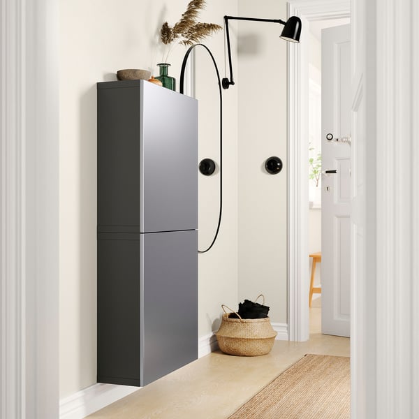 Moderner grauer Wandschrank, minimalistisches Design, mit zwei Türen, einem Weidenkorb und einer Wandleuchte in einem minimalistischen Raum.