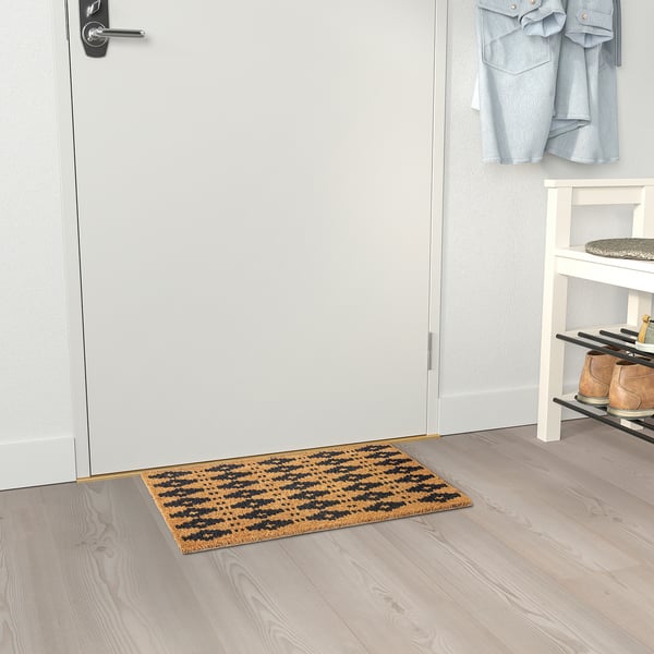 Eine braun-schwarz gestreifte Fußmatte befindet sich im Inneren einer Tür, fängt Schmutz effektiv auf und verbindet sich mit einem Schuhregal, wodurch die Sauberkeit im Eingangsbereich verbessert wird.