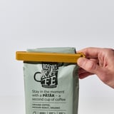 Die Hand schließt den gelben Clip am Kaffeebeutel, versiegelt ihn und sorgt für Frische.
