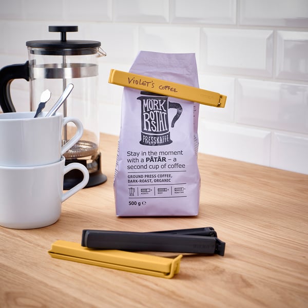 Versiegelter Kaffeebeutel mit Clips auf einer Theke. Inklusive französischer Presse und Tassen.