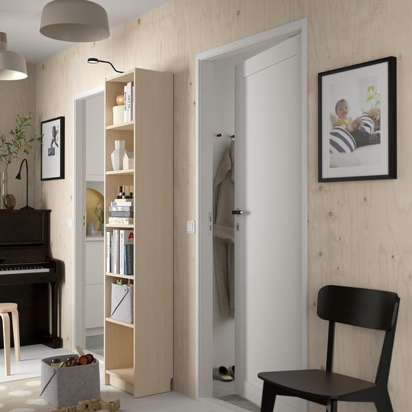 Modernes Zimmer mit BILLY Bücherregal, Kleiderschrank, schwarzem Stuhl und Klavier.