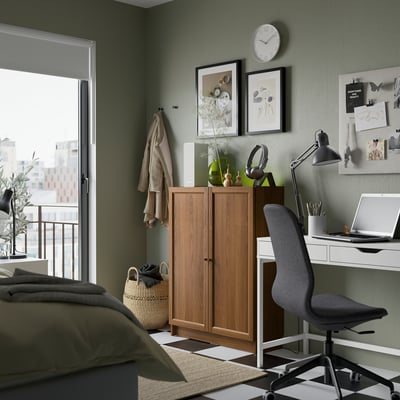 Gemütliches Schlafzimmer mit BILLY Bücherregal, Schreibtisch, Stuhl, olivgrüner Bettwäsche und grüner Wand mit Kunst und Uhr.