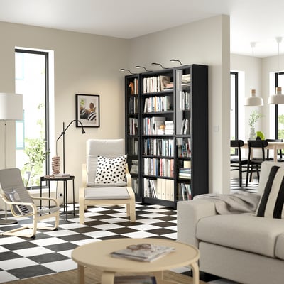 Modernes Wohnzimmer mit schwarzem Bücherregal BILLY, weißen Möbeln, kariertem Boden, großem Fenster und Pendelleuchten.