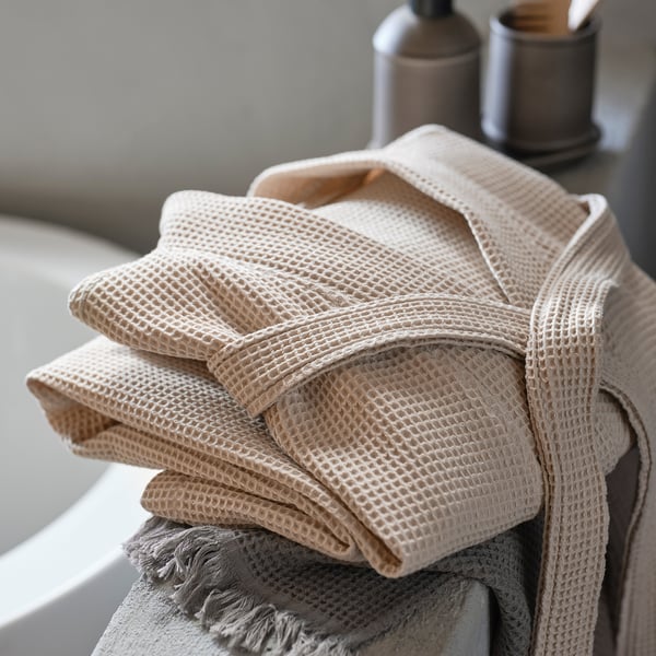 Gefalteter beiger BJÄLVEN-Bademantel auf dem Ständer, weiche Waffelstruktur, 80 % Baumwolle, 20 % Viskose.