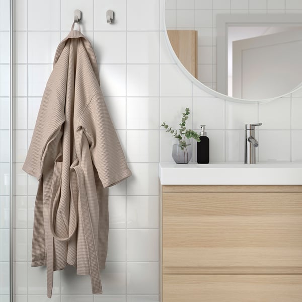 Beigefarbener Bademantel mit verstellbarem Gürtel hängt an einem Wandhaken im Badezimmer.