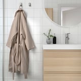 Beigefarbener Bademantel mit verstellbarem Gürtel hängt an einem Wandhaken im Badezimmer.