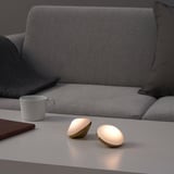 Zwei kleine dekorative Lichter auf einem Tisch neben einer grauen Couch und einer weißen Tasse, die ein warmes Licht ausstrahlen.