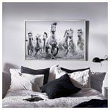 Ein stilvolles Schlafzimmer mit einer großen schwarz-weißen Wandkunst von rennenden Pferden über einem Bett mit grauen und weißen Kissen.