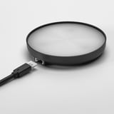 Kreisförmiges kabelloses Ladegerät, schlankes Design, schwarz mit dezenten konzentrischen Kreisen, verbunden über ein USB-Kabel.