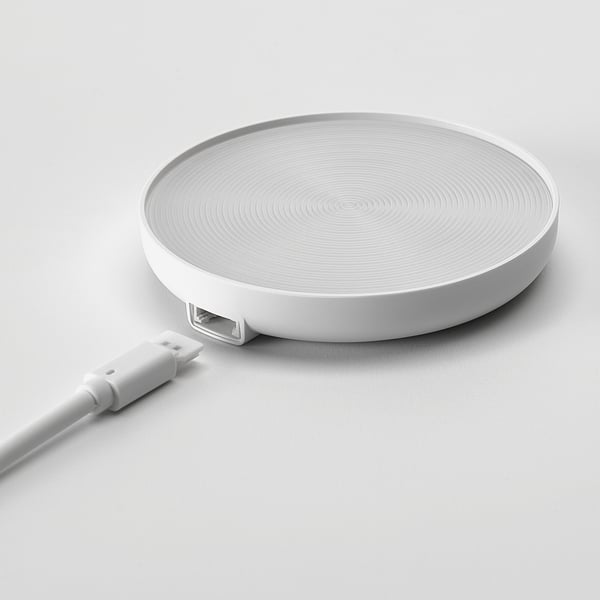 Flaches, weißes Ladepad mit wirbelnden Mustern. USB-Kabel angeschlossen, bereit für das kabellose Laden.