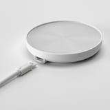 Flaches, weißes Ladepad mit wirbelnden Mustern. USB-Kabel angeschlossen, bereit für das kabellose Laden.