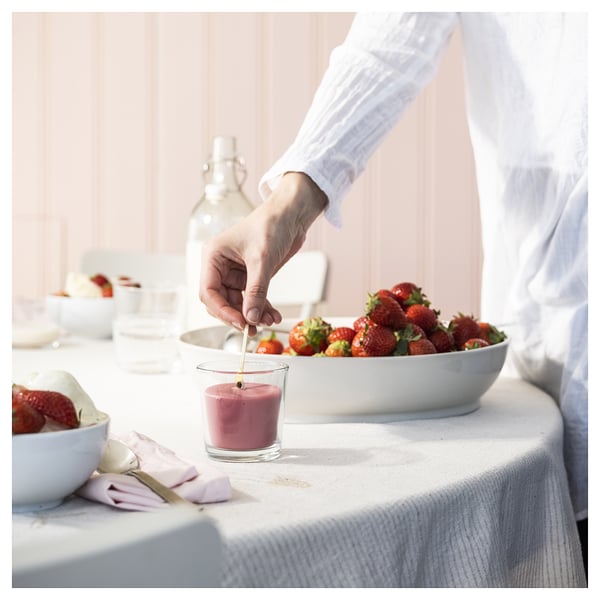 Die Person gießt rote Flüssigkeit in das Glas in der Nähe der Schüssel mit Erdbeeren auf dem Tisch.