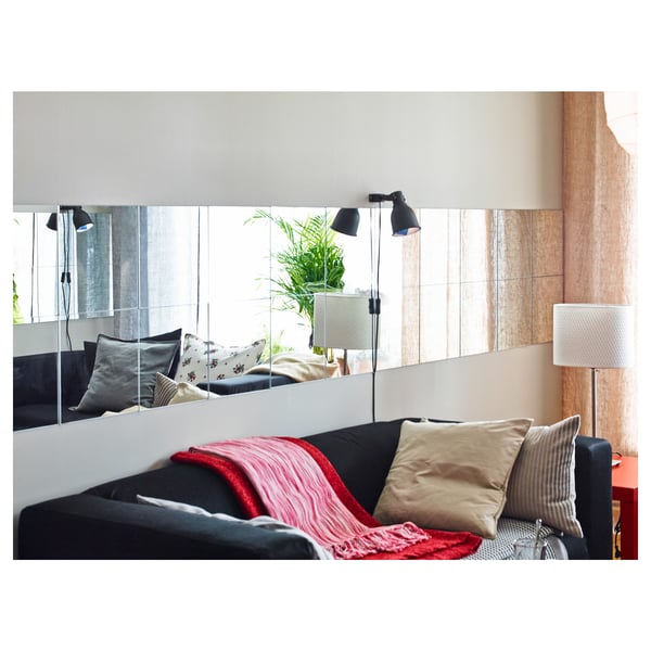 Modernes Wohnzimmer mit schwarzem Sofa, roter Decke, Wandlampen und verspiegelten Wandpaneelen, die ein geräumiges Gefühl schaffen.